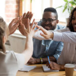 Group of diverse business people sitting at a table giving high fives