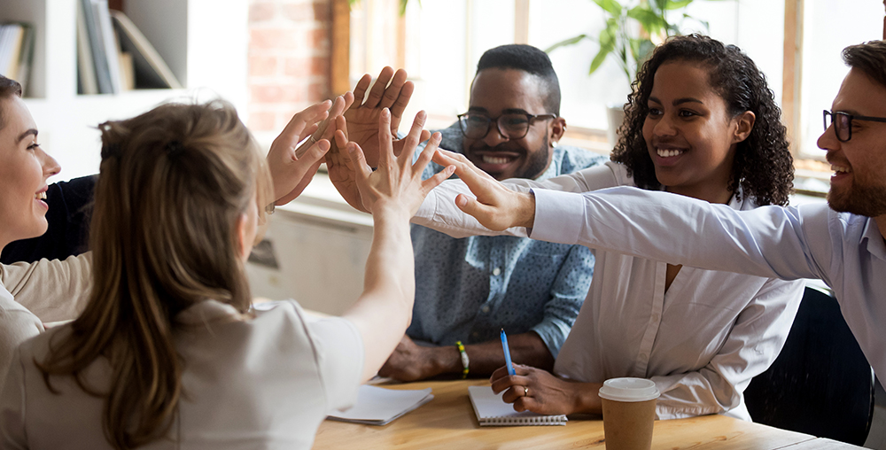 Group of diverse business people sitting at a table giving high fives