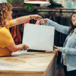 two smiling women exchanging a bag during a retail purchase