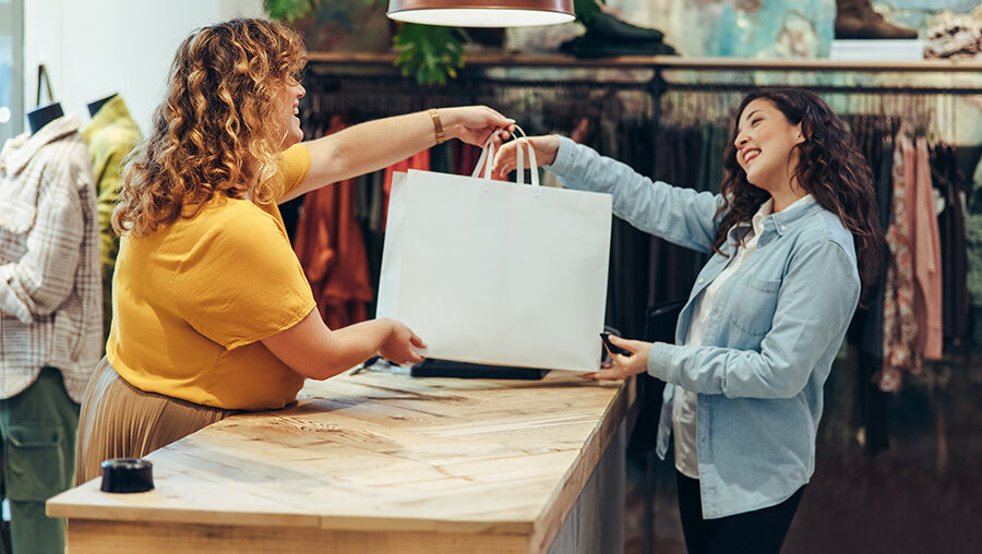 two smiling women exchanging a bag during a retail purchase