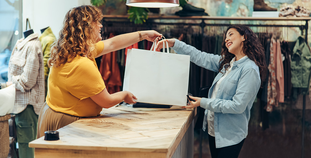 two smiling women exchanging a bag during a retail purchase