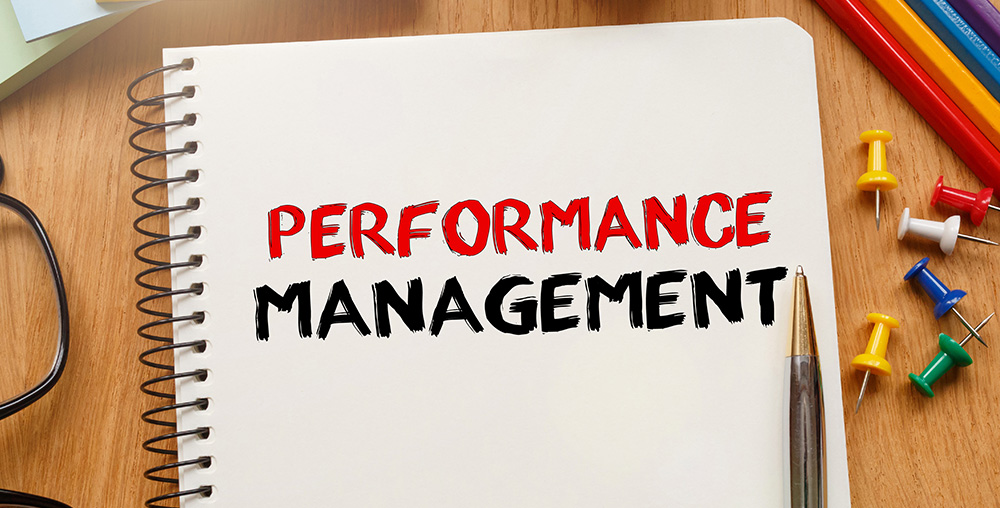 performance management written in notebook with pencil and push pins surrounding it