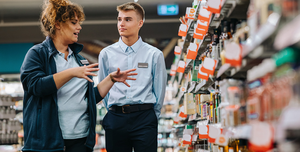 two retail employees talking in store aisle.