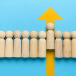 wooden figure blocks with one rising on a yellow up arrow